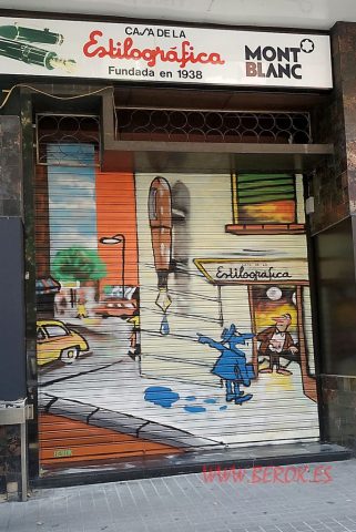 Graffiti artístico en persiana de tienda Casa de la Estilográfica con escena urbana, pluma estilográfica gigante y personajes caricaturescos.