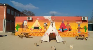 Mural infantil temático de indios y tipis pintado en la pared exterior de una escuela en Igualada