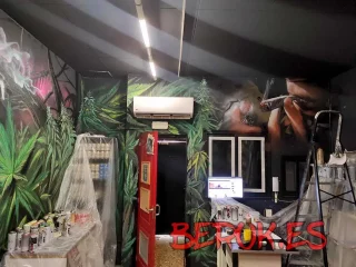 Mural decorativo en interior de asociación cannábica con hojas de cannabis, rostro fumando y ambiente artístico profesional
