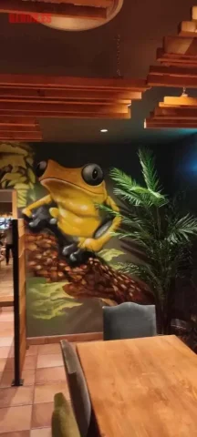 Mural de rana gigante pintada a mano en restaurante de Peralada graffiti de rana amarilla sobre rama en Croak’s Peralada
