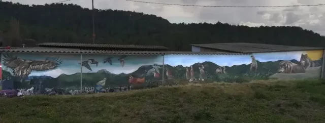 Graffiti mural en Berguedà con águila, buitres, lobos, caballos, cabras, perdices y aves en vuelo sobre paisaje de montaña.