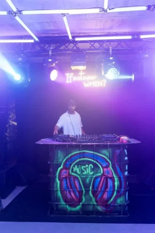 DJ en cabina decorada con graffiti y luces neón en evento corporativo