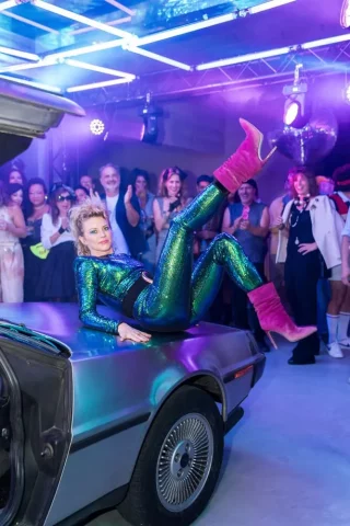 Fiesta temática 80s en Barcelona con mujer en traje brillante sobre DeLorean de Regreso al Futuro