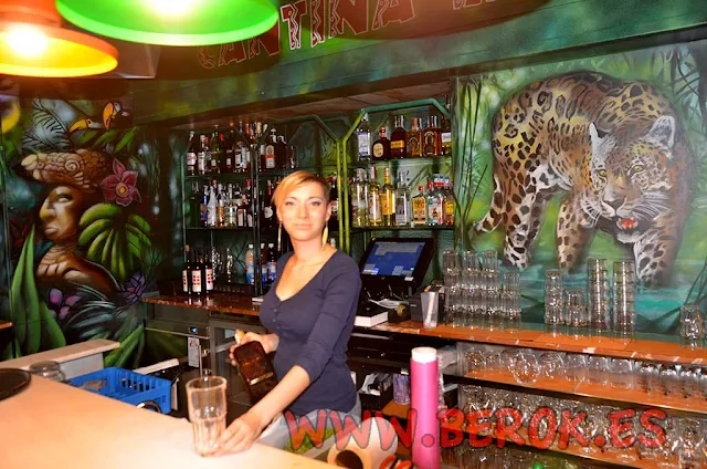 Mural cantina mexicana con jaguar, vegetación tropical y camarera en barra