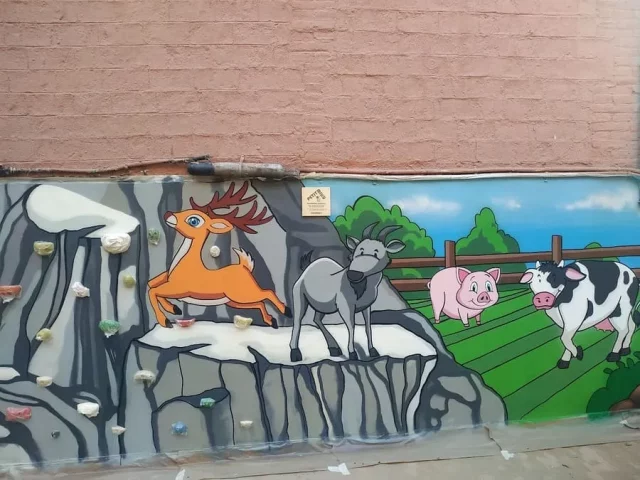 Animales y montañas en mural de rocódromo para escuela Mural infantil de animales y montañas junto a rocódromo escolar.