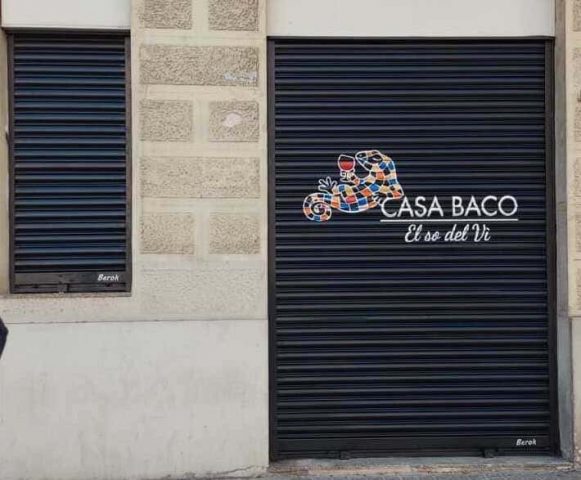 Graffiti en persiana de Casa Baco con logo mosaico y copa de vino sobre fondo negro Rotulación artística Casa Baco en persiana metálica