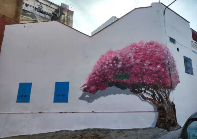 Mural exterior de árbol rosa estilo cerezo japonés. Mural de árbol rosa tipo cerezo japonés, jacaranda o lapacho rosado en fachada urbana.