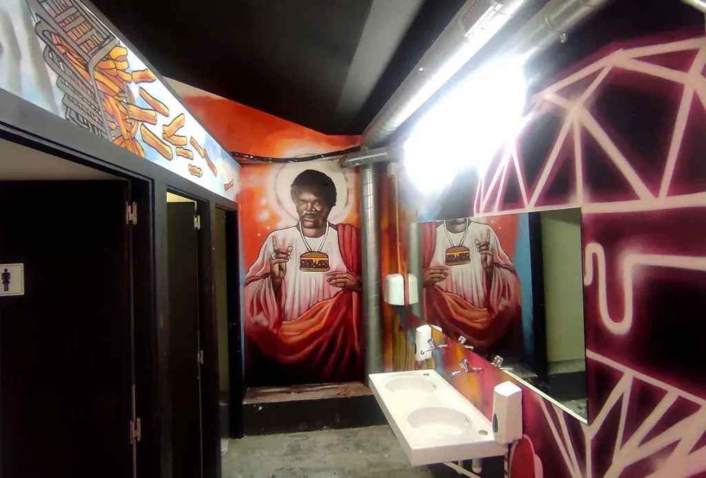 Graffiti mural artístico en lavabos de restaurante con personaje urbano y temática hamburguesa