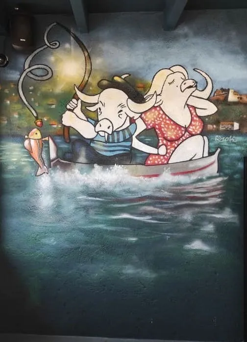 Graffiti estilo cómic con búfalos antropomorfos pescando en una barca sobre el agua