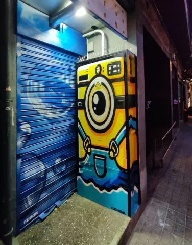 Graffiti de Kevin el minion de un ojo con forma de lavadora pintado en persiana metálica de lavandería en Barcelona