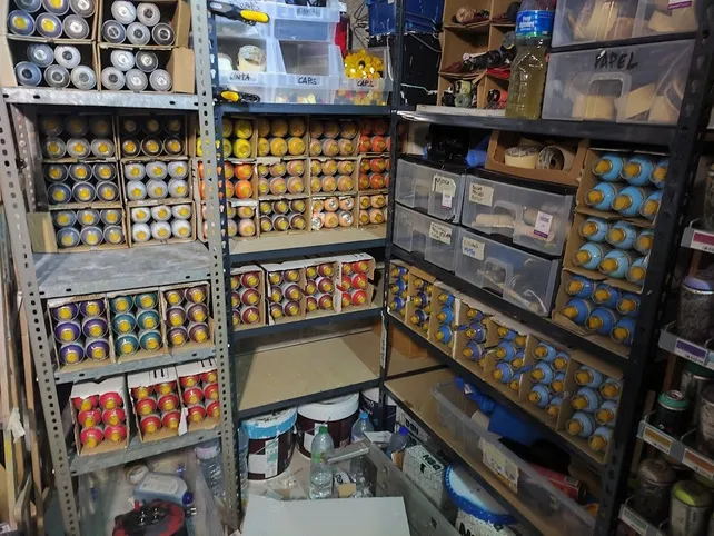 Estanterías con sprays de graffiti profesional de MONTANA COLORS (MTN), MONTANA CANS, BELTON MOLOTOW, IRONLAK, LOOP COLORS, KOBRA PAINT, NBQ, RUST-OLEUM, AEROPAK, PPG INDUSTRIES y AKZONOBEL organizados en un almacén de arte urbano.