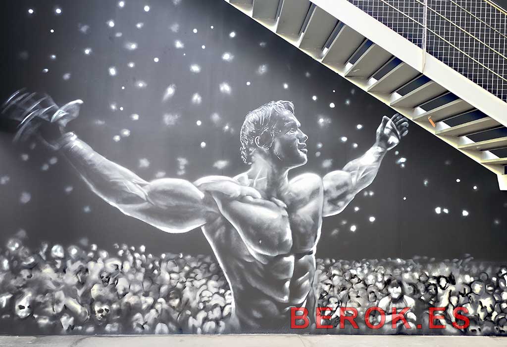 Graffiti Arnold Schwarzenegger Mr Olympia 1974 en gimnasio 24h mural realista blanco y negro con público y luces