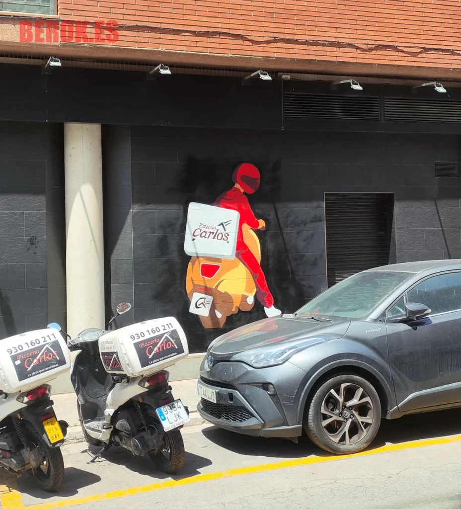 Graffiti repartidor en moto con logo Pizzería Carlos en fachada urbana