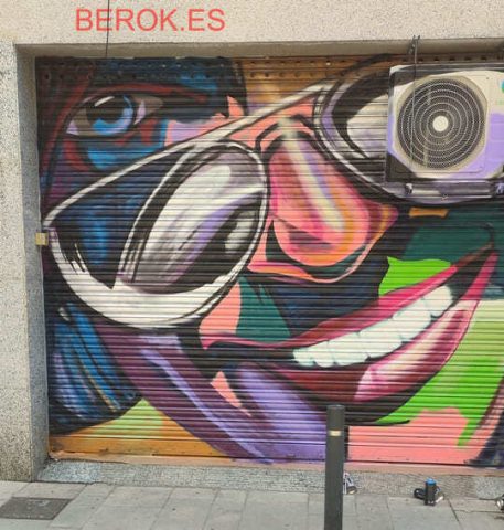 Graffiti pop art en persiana metálica con rostro femenino y gafas grandes en El Prat de Llobregat.