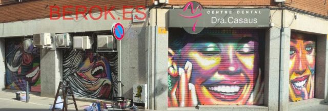 Graffiti artístico en persianas del Centre Dental Dra. Casaus con retratos urbanos de colores intensos en El Prat de Llobregat.