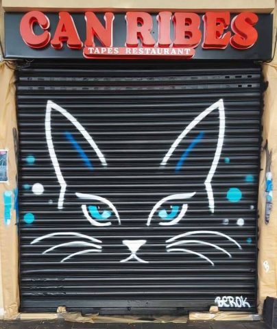 Graffiti de un gato con ojos azules pintado sobre la persiana del restaurante Can Ribes.