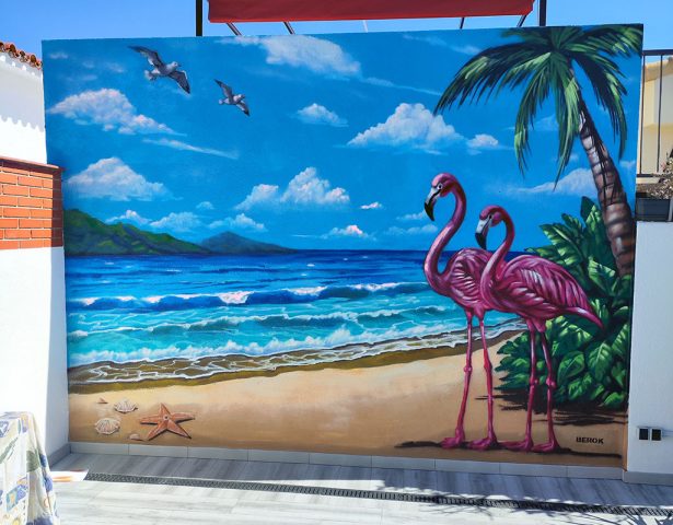 Mural decorativo de playa tropical con dos flamencos, mar, palmeras y cielo azul.