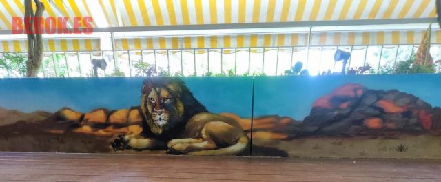 Graffiti mural de un león descansando en un paisaje desértico con rocas.