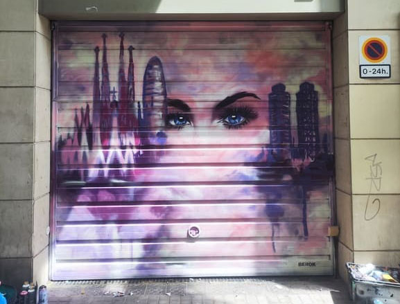 Graffiti de un rostro femenino con el skyline de Barcelona pintado sobre una persiana metálica.