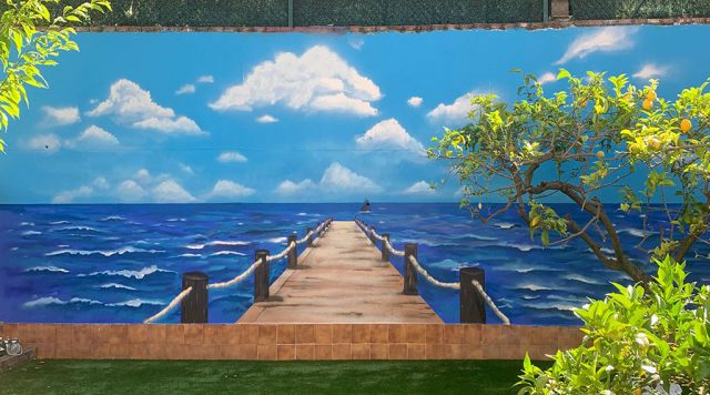 Mural con una pasarela de madera que se adentra en el mar creando un efecto de profundidad.