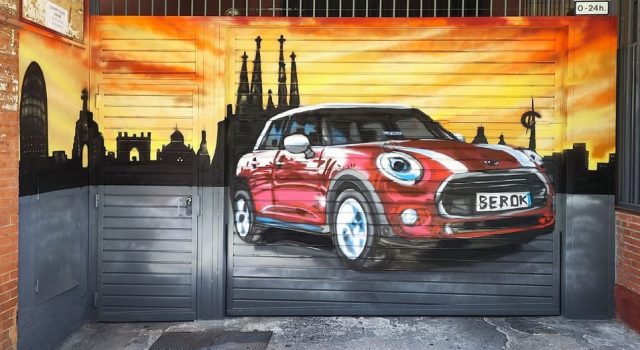 Graffiti de un Mini Cooper rojo sobre una puerta de garaje con el skyline de Barcelona al fondo.