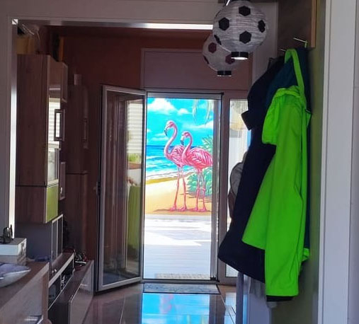 Vista desde el interior de una vivienda hacia un mural tropical con flamencos junto al mar.