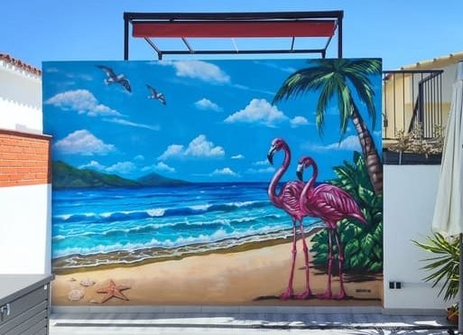 Mural tropical con flamencos, playa, mar, palmeras y cielo azul para terraza.