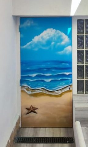 Puerta decorada con un mural de playa, mar, nubes y una estrella de mar en la arena.