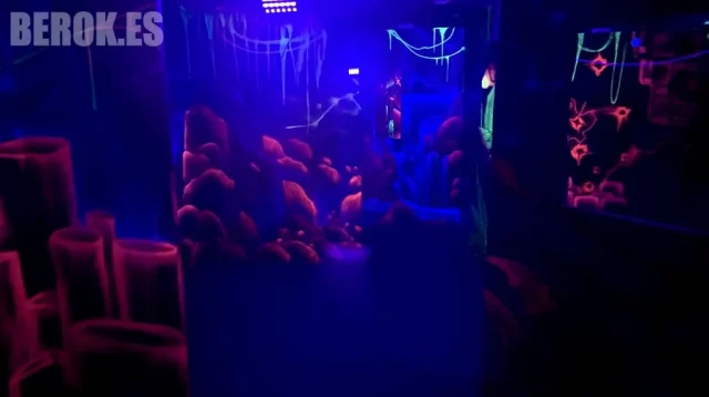 Ambientación Fluorescente de Sala Láser Tag con Formaciones Rocosas Sala de láser tag decorada con murales fluorescentes de rocas y formaciones bajo luz UV