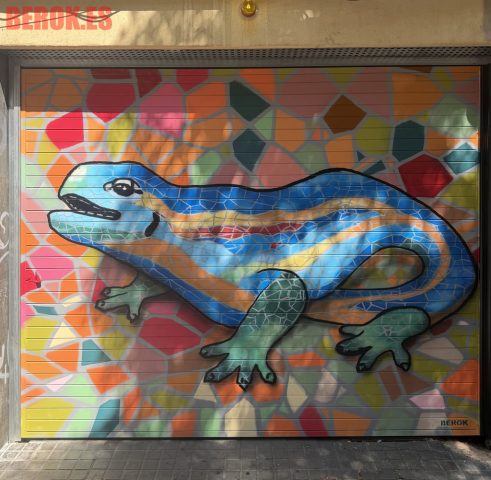 Graffiti en puerta de parking con la salamandra de Gaudí inspirada en el trencadís del Park Güell sobre un fondo de mosaico multicolor.