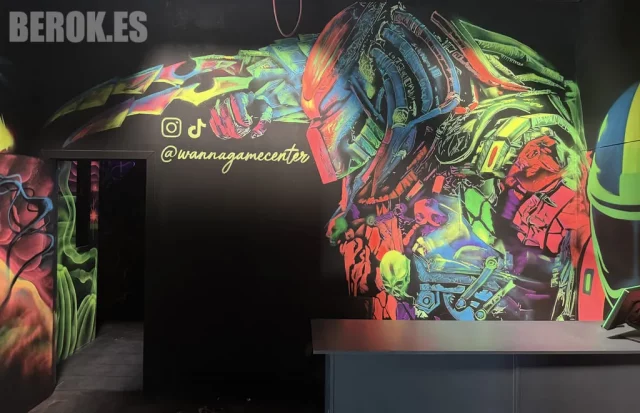 Mural Fluorescente de Predator en Zona de Recepción Mural fluorescente de Predator con detalles orgánicos y mecánicos en gaming center