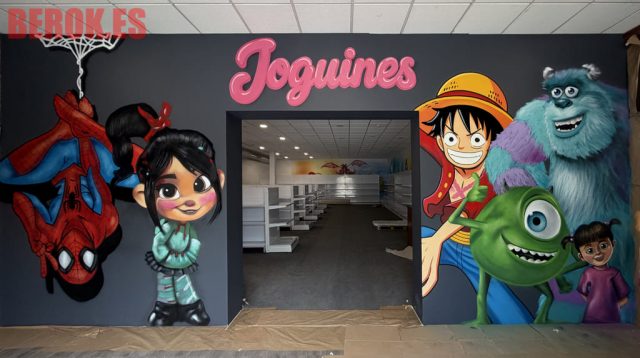 Mural para tienda de juguetes con Spider-Man, Vanellope, Luffy, Sulley, Mike Wazowski y Boo decorando la entrada junto al rótulo rosa "Joguines".