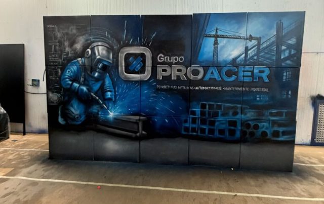 Vista general de un mural azul con un soldador, el logotipo de Grupo Proacer y estructuras industriales al fondo.