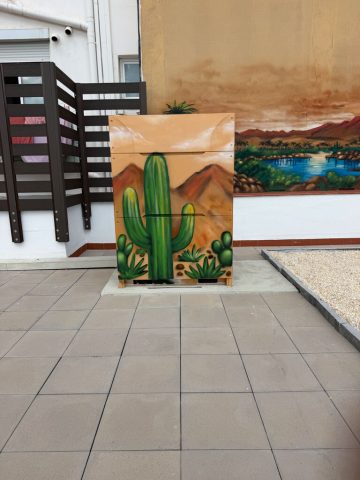 Cactus y desierto pintados en una caja de aire acondicionado Caja de aire acondicionado decorada con cactus, montañas y cielo de desierto en una terraza.