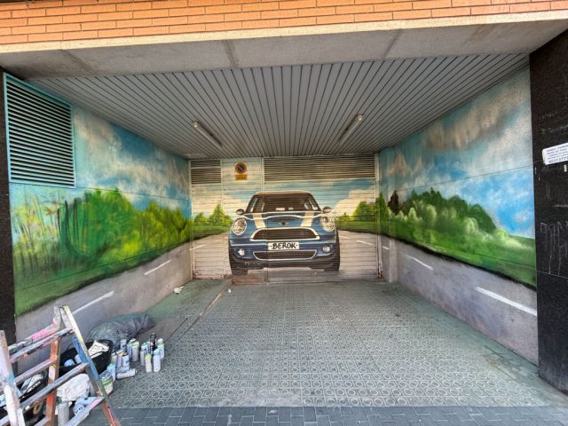 Mural de Mini Cooper y carretera en un garaje Garaje decorado con un coche Mini Cooper de frente al fondo y una carretera con vegetación y cielo en las paredes laterales.