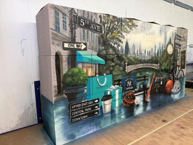 Mural con un parque, skyline de Nueva York, señales de la Quinta Avenida y objetos urbanos visto en perspectiva.