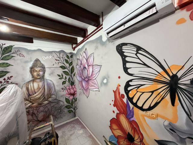 Buda y mariposa amarilla en murales de esquina Dos paredes contiguas decoradas con Buda entre flores de loto y un rostro femenino con una gran mariposa amarilla.
