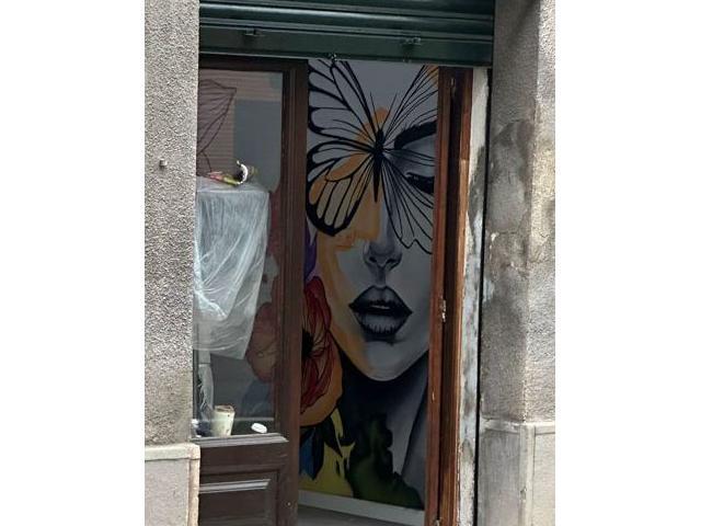 Entrada de un local desde la calle con murales de una mujer y mariposas visibles en el interior.