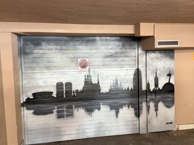 Puerta de garaje con skyline de Barcelona y reflejo Puerta de garaje pintada en blanco y negro con monumentos del skyline de Barcelona reflejados sobre el agua.